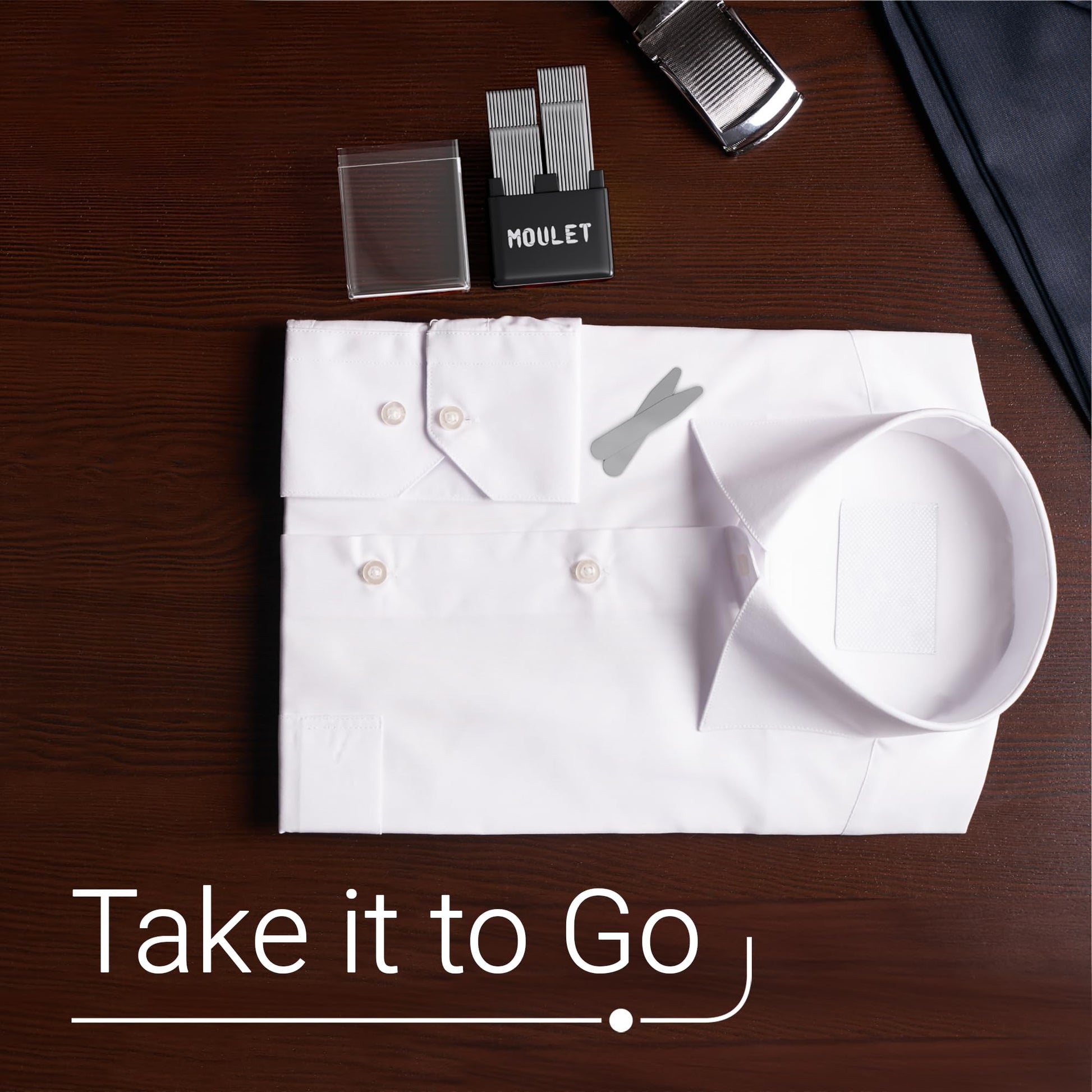 Folded white shirt with collar stays and  accessories on a wooden surface, featuring the brand 'MOULET'.